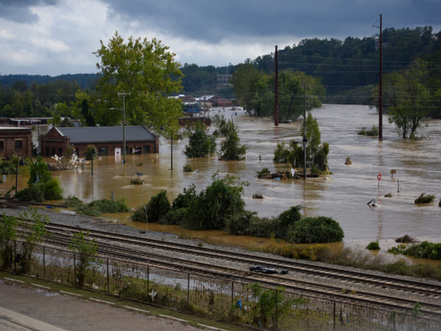 Severe flooding in Asheville, North Carolina after Hurricane Helene, showing submerged buildings and railway tracks.