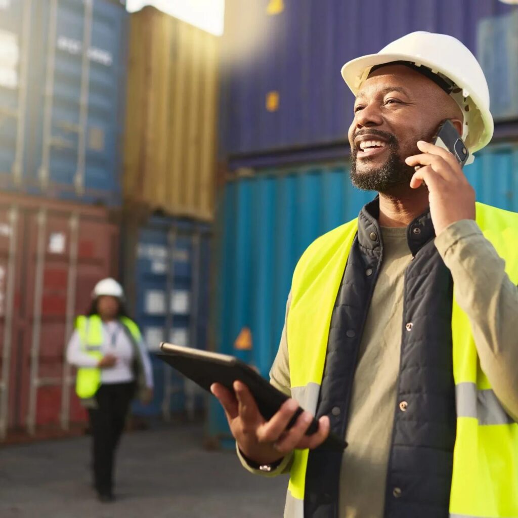 Man with hardhat and iPad smiling on phone and talking.
