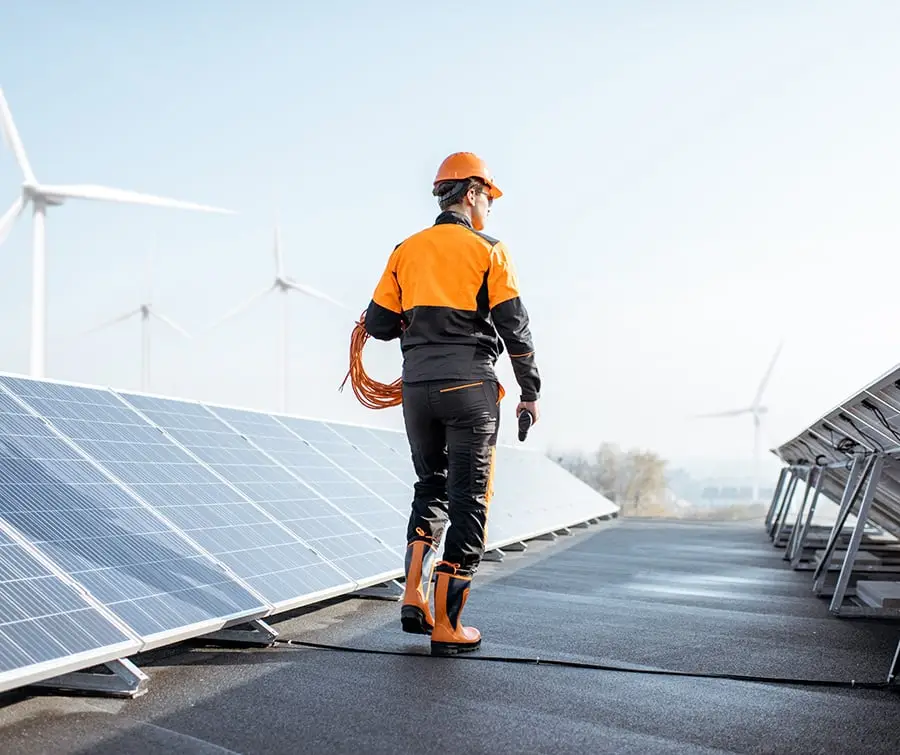 Man walking at energy site with solar panels and wind turbines.
