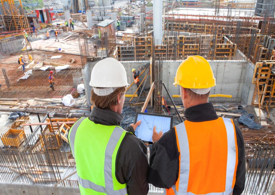 Construction site workers wearing hardhats overlooking construction of a large building in the city.
