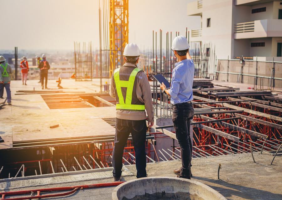 Construction site workers wearing hardhats overlooking construction of a large building in the city.