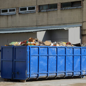 A large metal blue dumpster near the wall of the house
