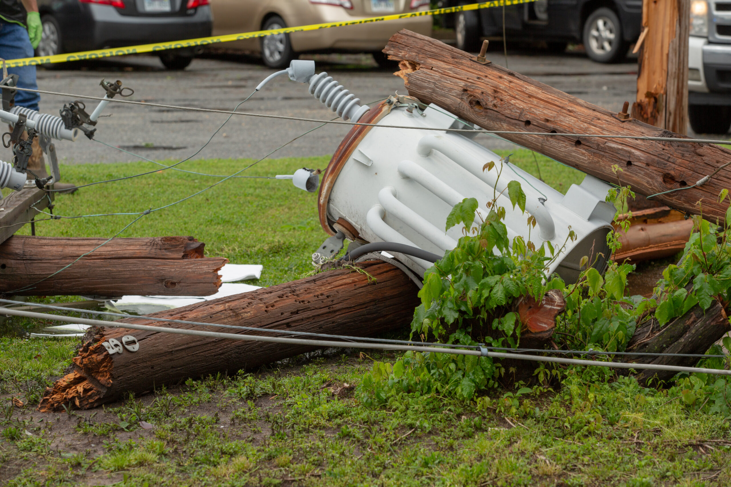 Downed utility pole and transformer with snapped wires after tornado, cordoned off with caution tape