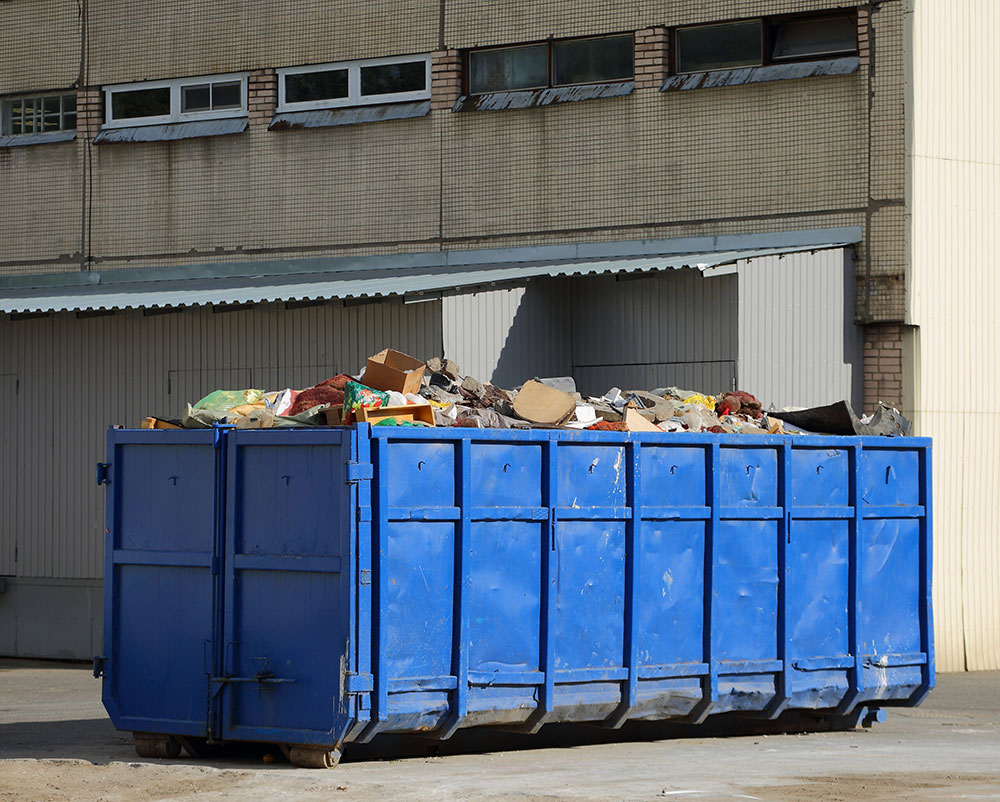 Empty roll-off dumpsters staged in a row behind a grocery store ahead of a storm.