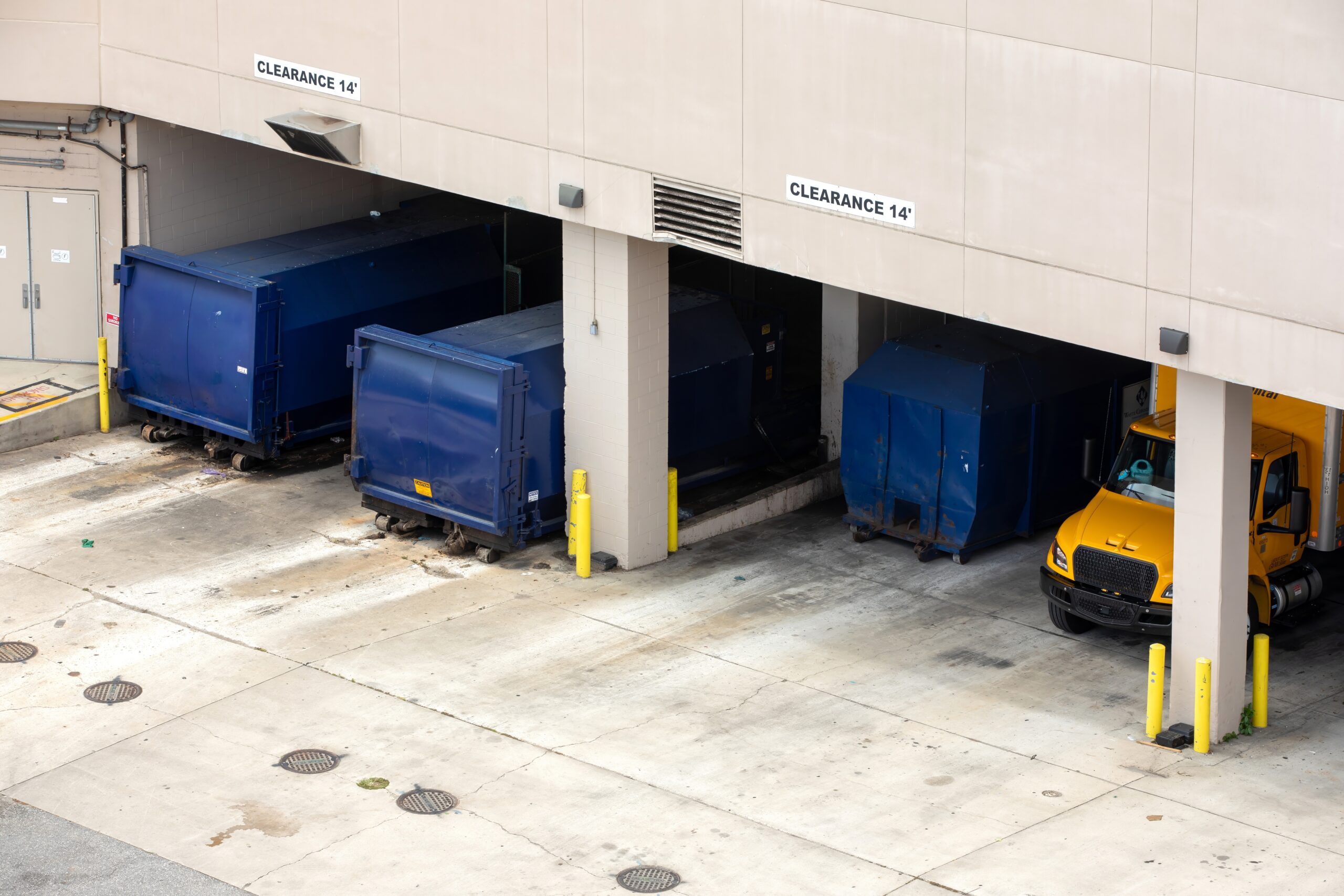 A stationary compactor and its receiver container docked behind a retail property.