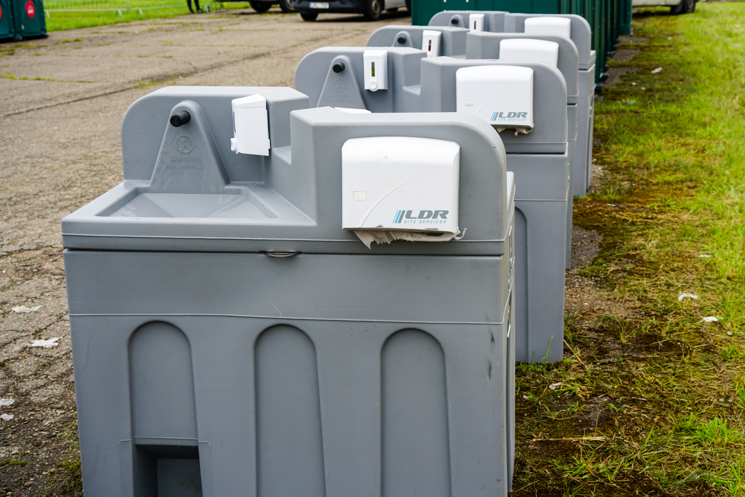 Two portable handwash stations beside a row of portable restrooms at a construction site.